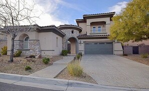 A two-story house with a stone facade, a garage, and a landscaped front yard. - Luxury 6BR Summerlin West Oasis Detached Casita Gated Community (Las Vegas)