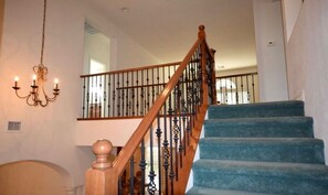 Eine Treppe mit hölzernem Geländer und schwarzen Spindeln, die zu einem Podest mit einer Chandelüster führt.