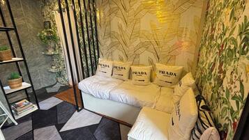 Un dormitorio moderno con un sofá cama, un papel tapiz estampado, una estantería y una planta decorativa.