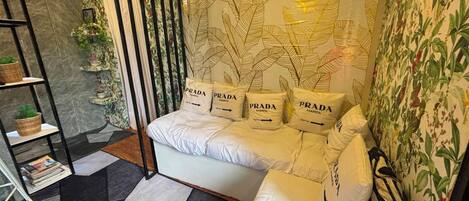 A modern bedroom with a sofa bed, a patterned wall, a bookshelf, and a decorative plant.