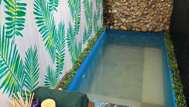 A small, enclosed outdoor area with a stone wall, a blue water feature, and a wall decorated with green leaf patterns.