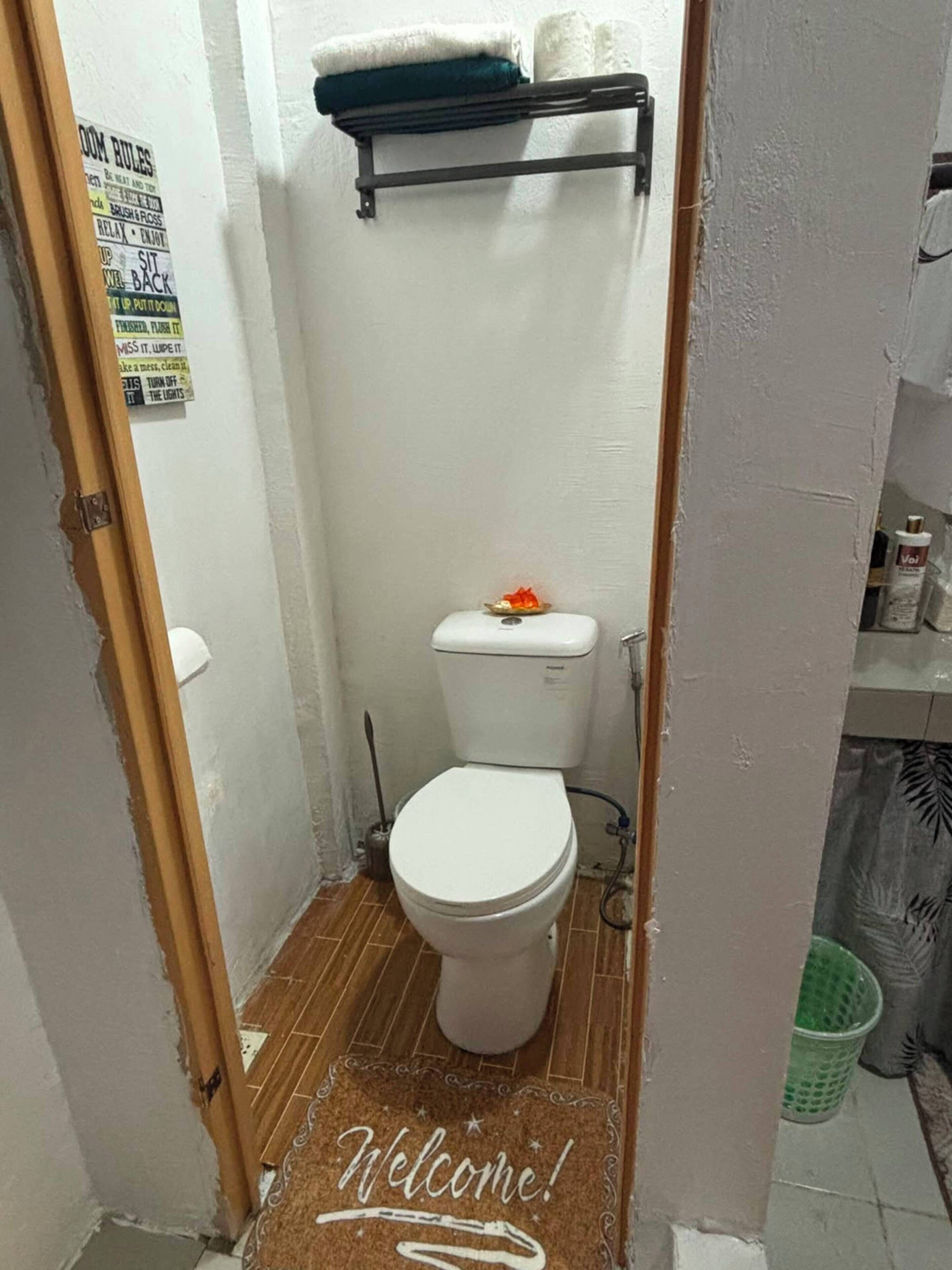 Ein kleines Badezimmer mit Toilette, einer Fußmatte, einem Ablagefächer mit Handtüchern und einem an der Wand befestigten Schild.