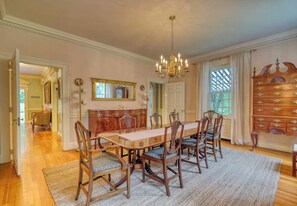 Una sala de dinar elegant amb una taula de fusta llarga, sis cadires, un penjador de cristall, un mirall i un armari de fusta amb calaixos.