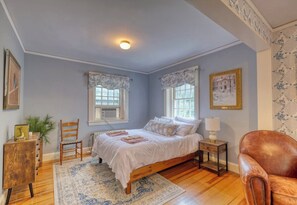 A bedroom with a wooden bed, two bedside tables, a chair, a floor lamp, and a window with a view.