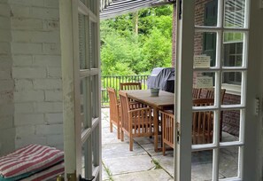 Un portico coperto con tavolo e sedie, un barbecue e vista su un giardino verde.