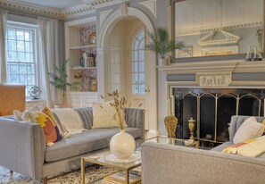 A living room with a sofa, armchairs, a fireplace, and a bookshelf. - Grand Berkshire Manor By Evergreen Home (Pittsfield)