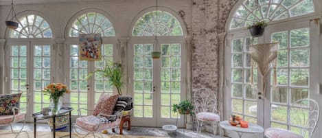 A room with arched windows, a table with a vase of flowers, and a chair with a cushion.