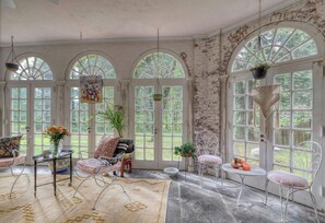 A room with arched windows, a table with a vase of flowers, and a chair with a cushion.