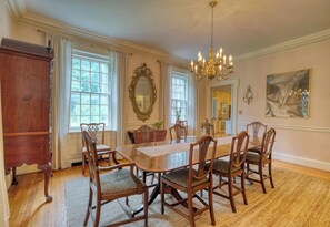 A dining room with a long wooden table, six chairs, a chandelier, and a large mirror on the wall.