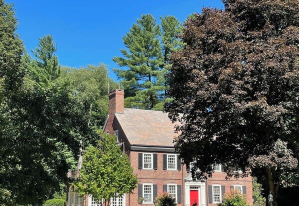 A traditional brick building with a red door, surrounded by trees and a clear blue sky.