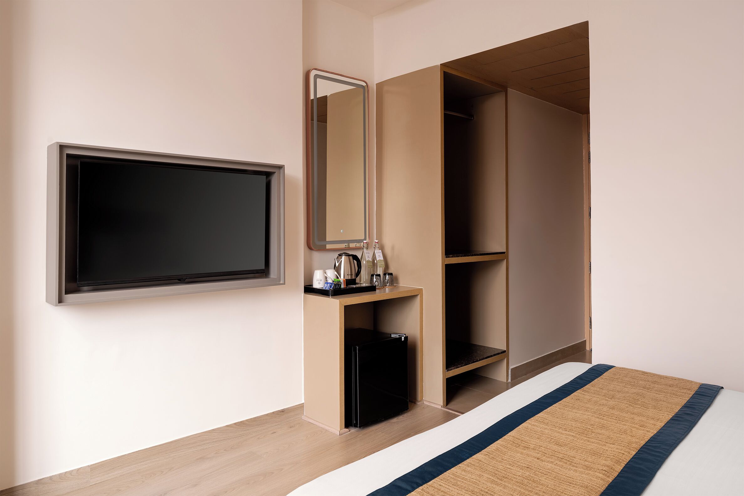 Quarto de hotel com cama, televisão, guarda-roupa e uma pequena escrivaninha com chaleira e chávenas.