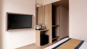 Quarto de hotel com cama, televisão, guarda-roupa e uma pequena escrivaninha com chaleira e chávenas.