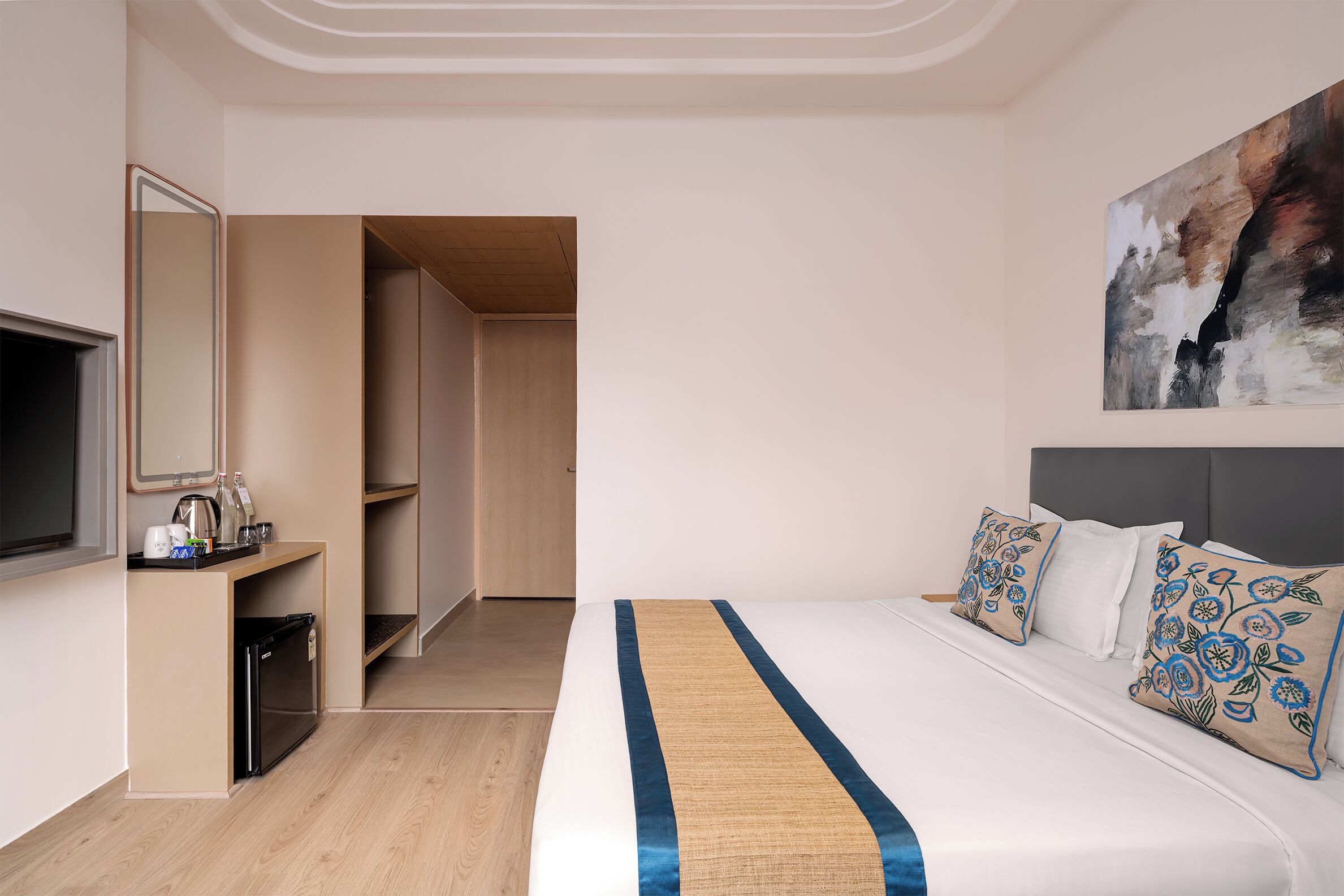 Quarto de hotel com uma cama, televisão, cafeteira e porta que dá para um corredor.