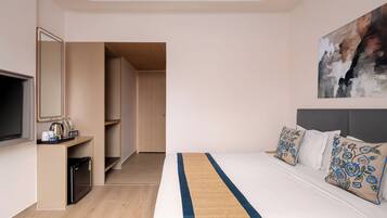 Quarto de hotel com uma cama, televisão, cafeteira e porta que dá para um corredor.