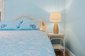 A bed with a blue patterned bedspread and pillows, a white wicker nightstand with a lamp, and a wicker chair. - 2-Acre Retreat Near Ocean City + Game Room (Berlin)