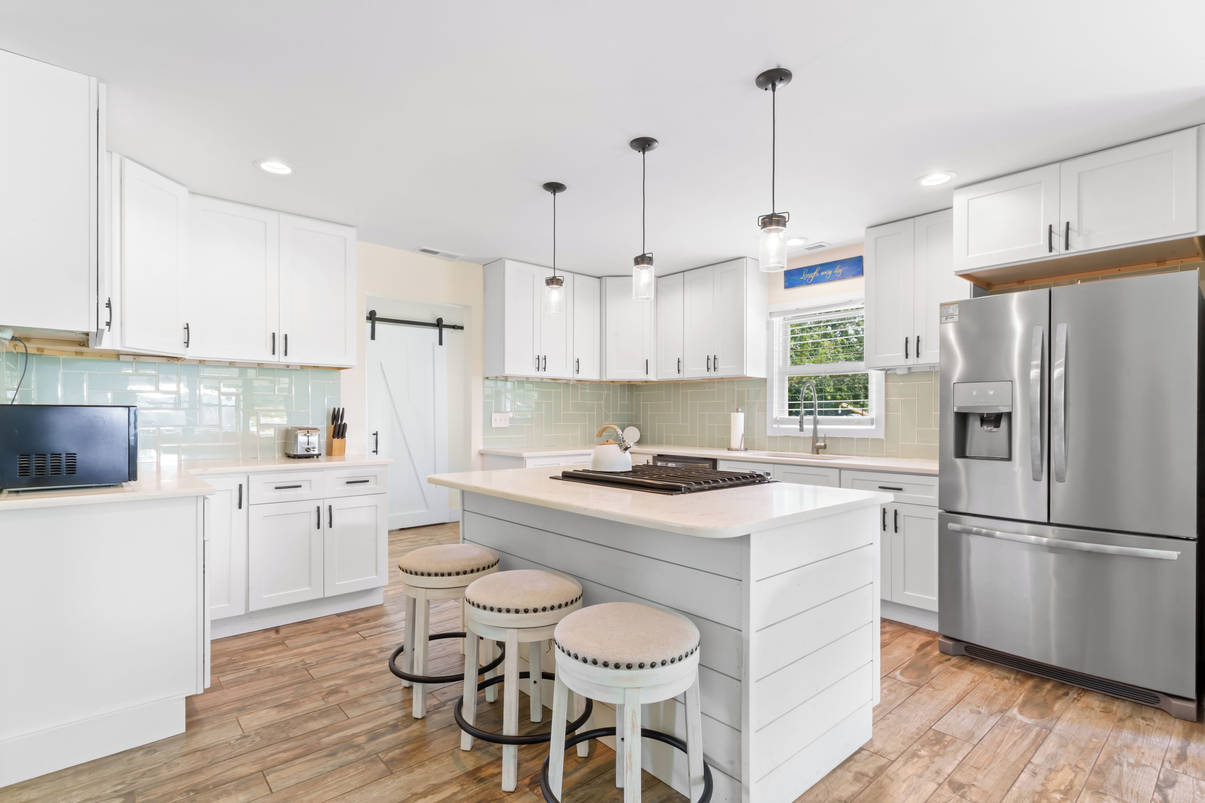 A modern kitchen with white cabinets, a stainless steel refrigerator, and a central island with stools.