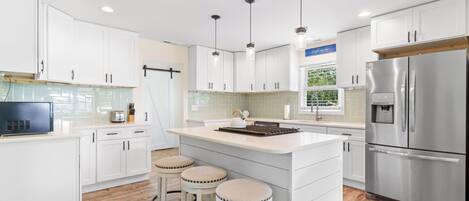 A modern kitchen with white cabinets, a stainless steel refrigerator, and a central island with stools.