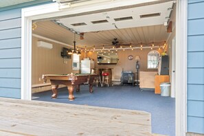 Ein Billardtisch in einem Raum mit Deckenventilator, Lichterkette und einem Holzfass.