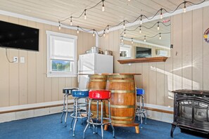 A room with wooden walls, a bar area with stools, a refrigerator, and a television mounted on the wall. - 2-Acre Retreat Near Ocean City + Game Room (Berlin)