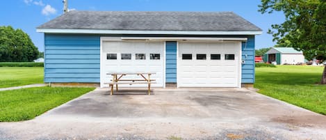 A single-story building with a garage, a picnic table, and a grassy area in front.