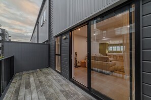 A modern building with a balcony, large sliding glass doors leading to a living area with a sofa and a dining table. - Modern Christchurch 4BR w/ Balcony Near NZ Stadium (Christchurch)