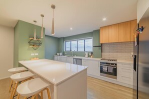 A modern kitchen with a central island, wooden cabinets, a stainless steel refrigerator, and a window providing natural light. - Modern Christchurch 4BR w/ Balcony Near NZ Stadium (Christchurch)