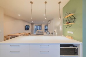Eine moderne Küche mit Kochinsel, Essbereich mit Tisch und Stühlen, einer Couch und einer geometrischen Wanddekoration.