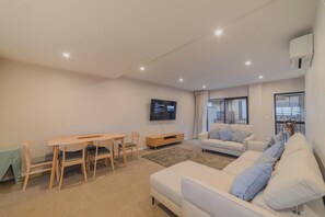 Ein modernes Wohnzimmer mit Sofa, Esstisch, Stühlen, Fernseher und Blick auf die Stadt durch das Fenster.