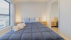 Hotellihuone, jossa on suuri sänky, kaksi yöpöytää valaisimineen, suuri peili ja näkymä ikkunasta.