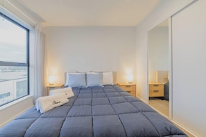 Ein Hotelzimmer mit einem großen Bett, zwei Nachttischen mit Lampen, einem großen Spiegel und Blick aus dem Fenster.