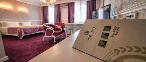 A hotel room with a bed, a chair, a desk, and a chandelier.
