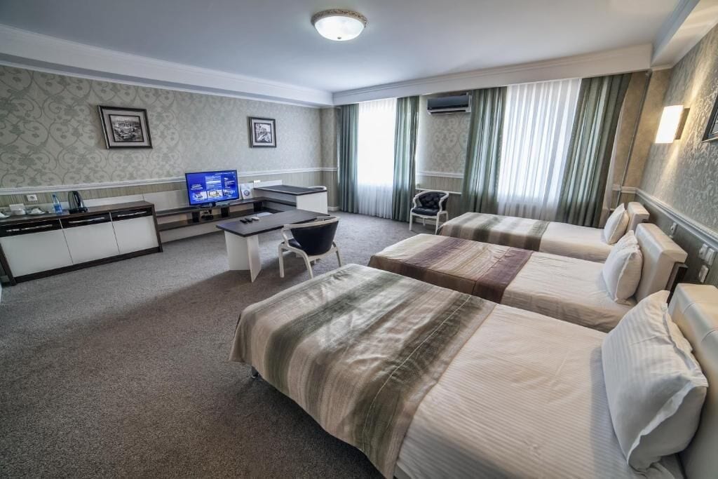 A hotel room with two beds, a desk with a computer, a chair, and a television.