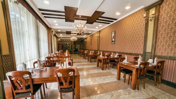 Uma sala de jantar de hotel com várias mesas e cadeiras, parede estampada e um candelabro.