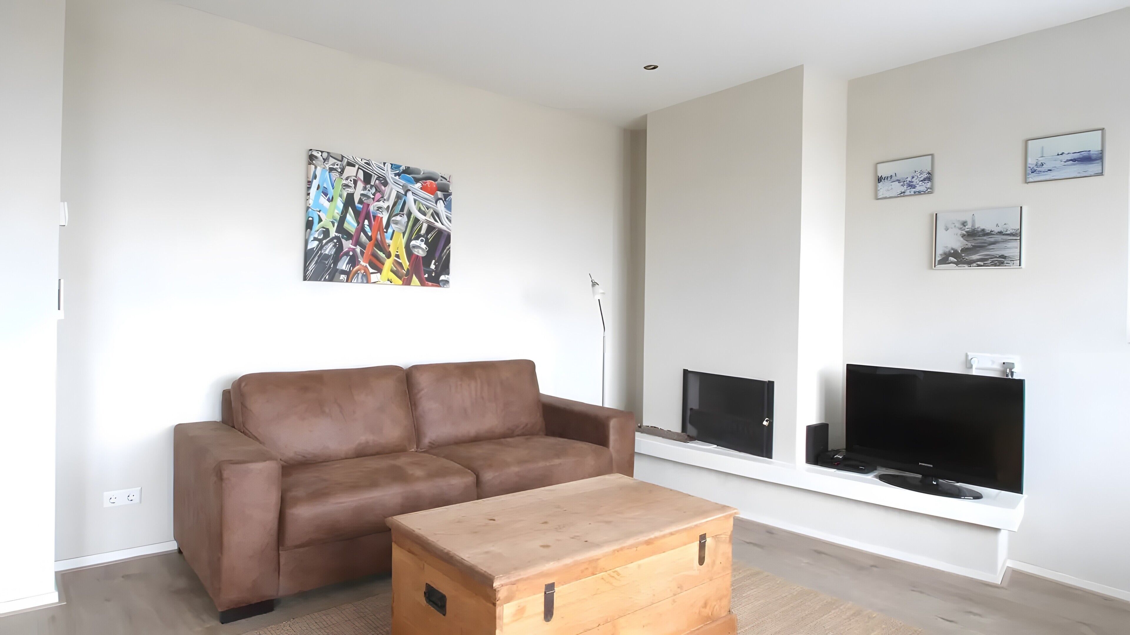 Ein modernes Wohnzimmer mit einer braunen Couch, einem Holztisch, einem Flachbildfernseher und einem Bild an der Wand.