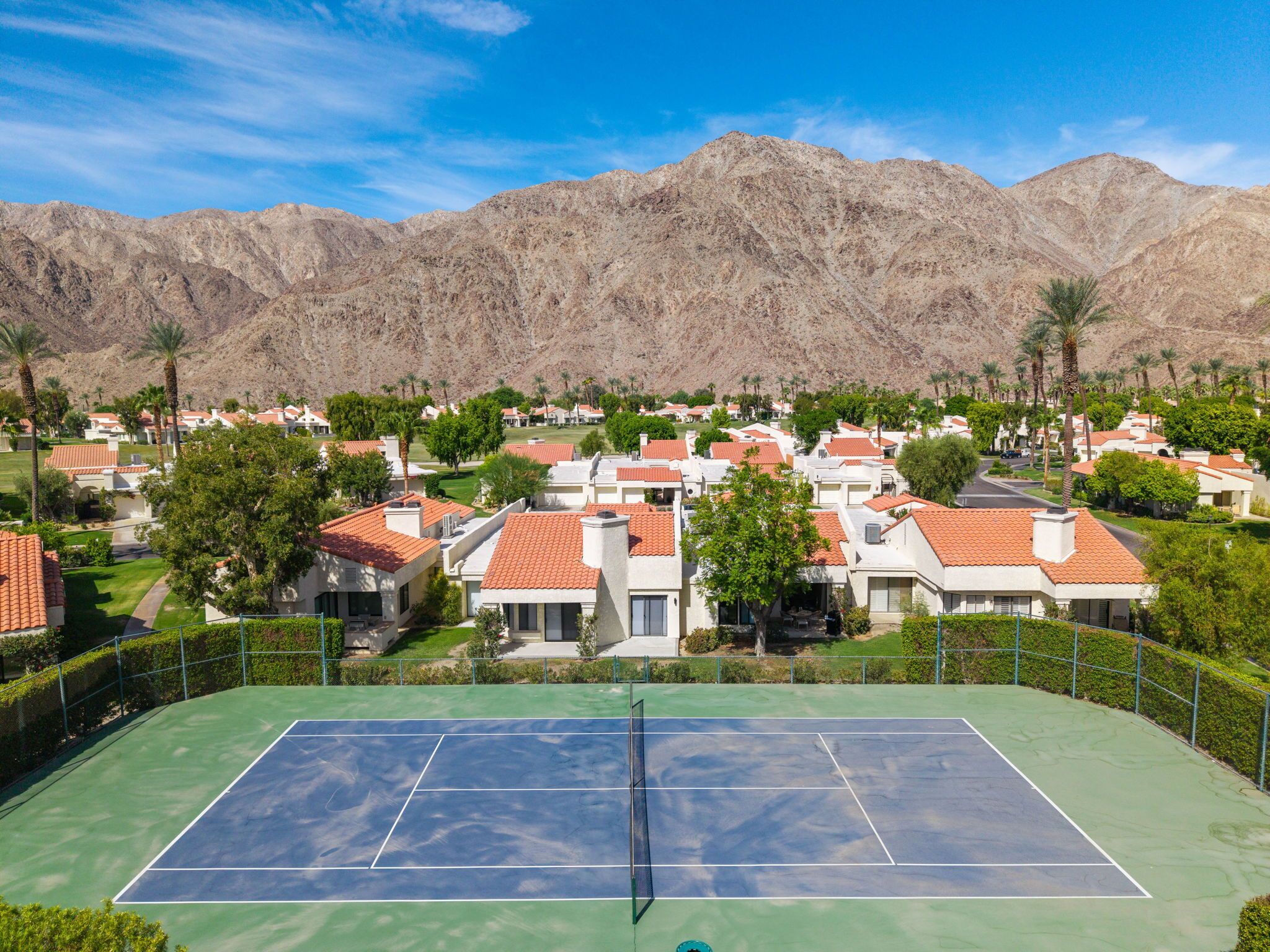 A residential area with houses, a tennis court, and mountains in the background.