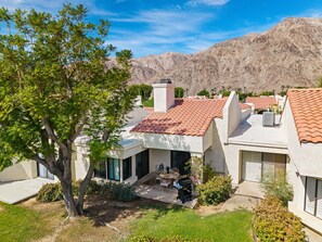 A residential area with houses featuring red-tiled roofs, a tree in the foreground, and mountains in the background. - Santa Rosa Cove #078 2BD, 2BA, 1389 sqft (La Quinta)