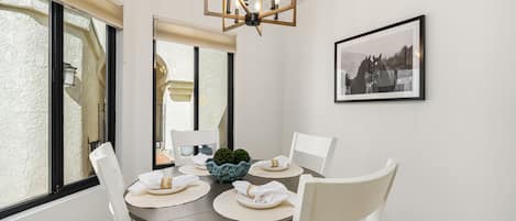 A dining area with a round table, white chairs, a chandelier, and a framed picture on the wall.