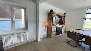 Een keuken met een houten kast, een radiator, een eettafel en een raam met zonwering.