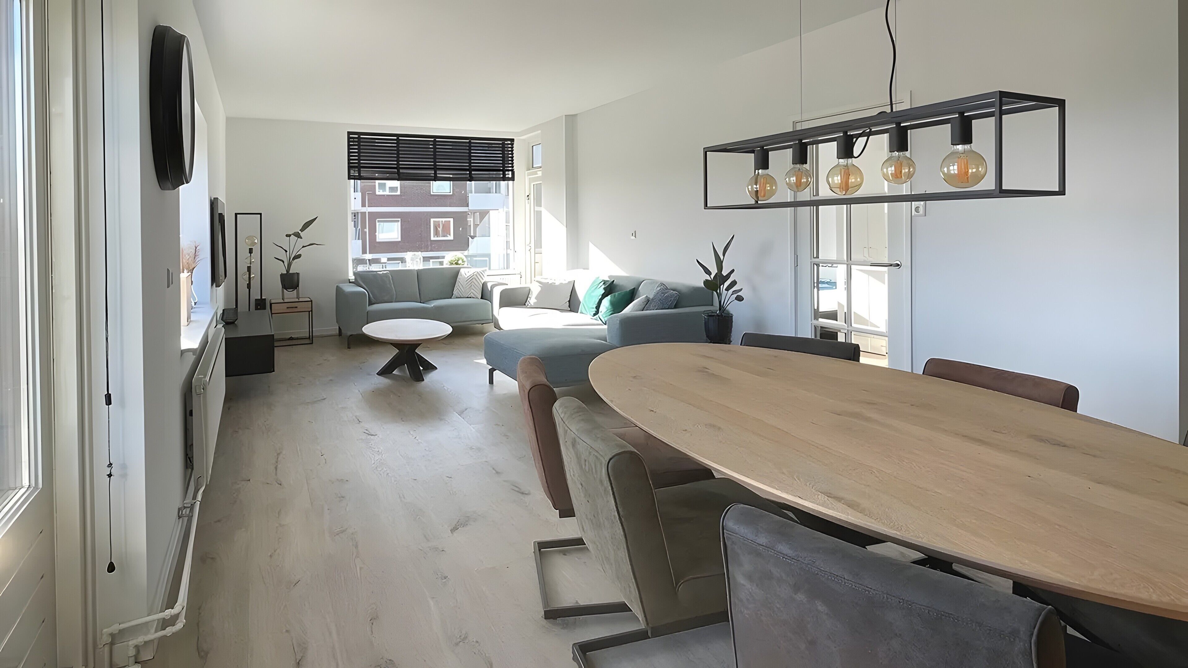 A modern living room with a dining area, a sofa, a coffee table, and a kitchen visible in the background.