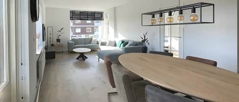 Een moderne woonkamer met een eethoek, een bank, een bijzettafeltje en een keuken in de achtergrond.