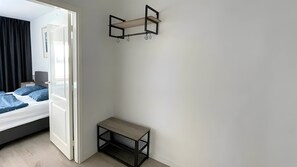 A room with a bed, a small table, a wall-mounted shelf, and a door leading to another room.
