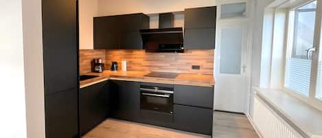 Una cocina moderna con armarios negros, encimera de madera y horno empotrado.