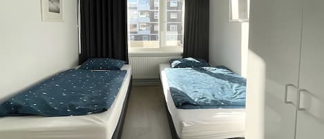 Una habitación con dos camas individuales, una ventana con cortinas, un radiador y un cuadro en la pared.