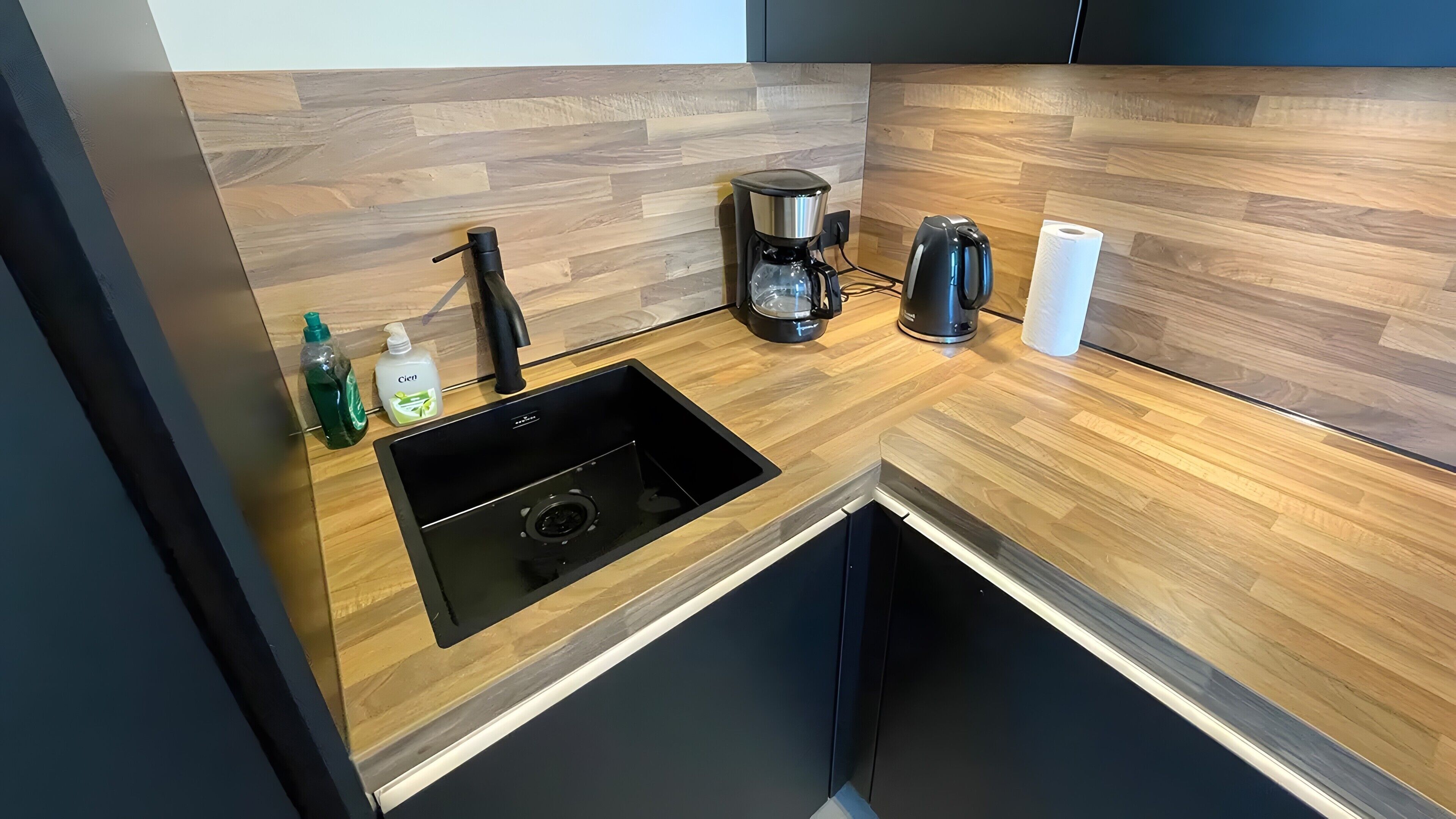 Eine moderne Küche mit einer Holz Arbeitsplatte, einem schwarzen Spülbecken, einer Kaffeemaschine und einem Papiertuchspender.