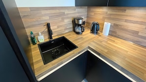 Een moderne keuken met een houten aanrecht, een zwarte spoelbak, een koffiezetapparaat en een keukenrolhouder.