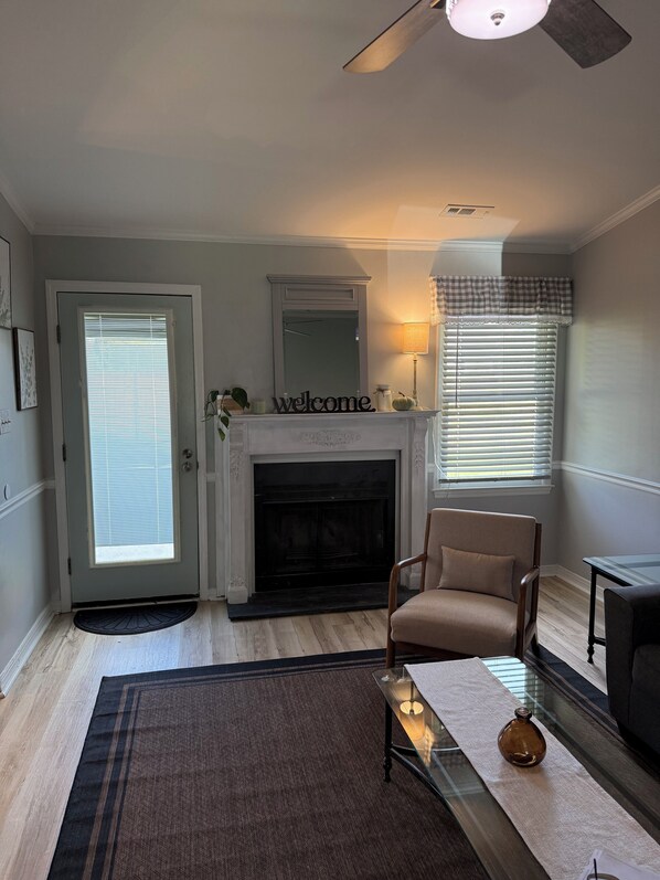 A living room with a fireplace, a chair, a coffee table, and a door with blinds. - Timber Time (Havelock)