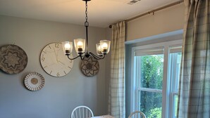 A dining room with a wooden table, white chairs, a wall clock, and a chandelier. - Timber Time (Havelock)