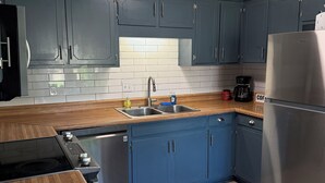 A modern kitchen with blue cabinets, a stainless steel refrigerator, a wooden countertop, and a built-in dishwasher. - Timber Time (Havelock)