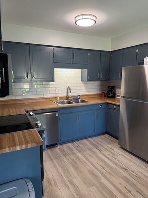 Eine moderne Küche mit blauen Schränken, einem Edelstahlkühlschrank, einer Holz Arbeitsplatte und einem eingebauten Geschirrspüler.
