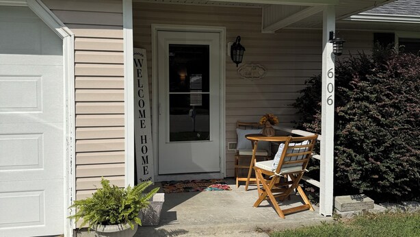 A house with a stone facade, a white garage door, a front porch with a table and chairs, and a mailbox. - Timber Time (Havelock)